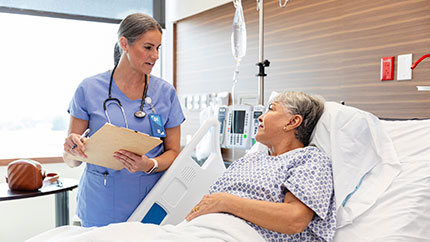 Healthcare provider checking on an elderly patient lying in hospital bed.